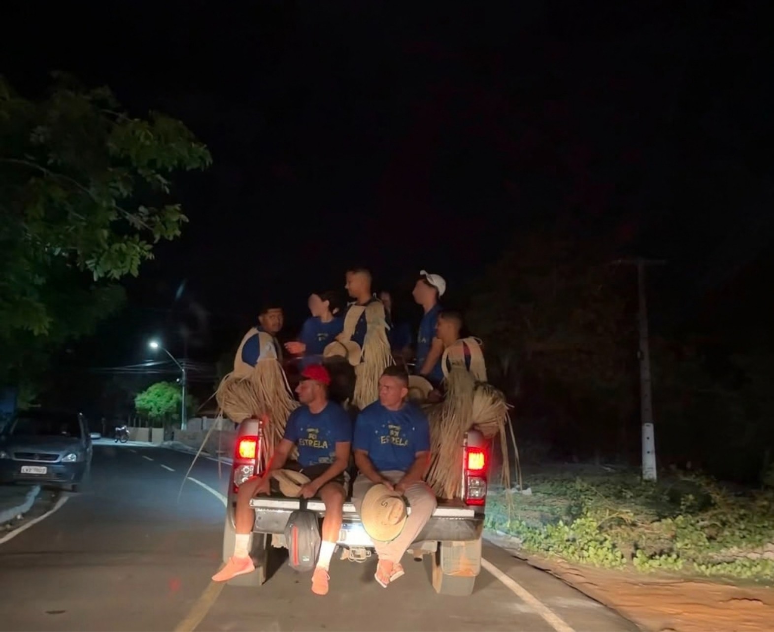 Integrantes do Boi Estrela em uma carroceria aberta durante deslocamento noturno por estrada na zona rural de Boa Hora-PI; alguns usam camisas azuis e indumentárias de palha.